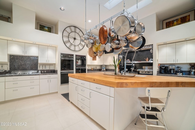 kitchen with a skylight, wood counters, tasteful backsplash, black double oven, and white cabinets