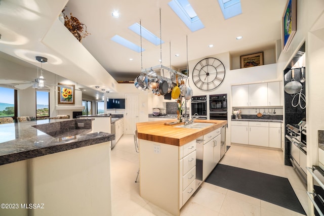 kitchen featuring wooden counters, a skylight, ceiling fan, a kitchen island, and white cabinetry