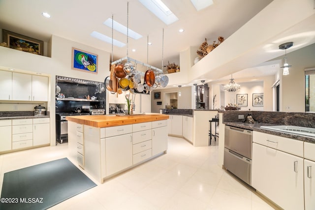 kitchen featuring a high ceiling, wooden counters, white cabinets, hanging light fixtures, and a skylight