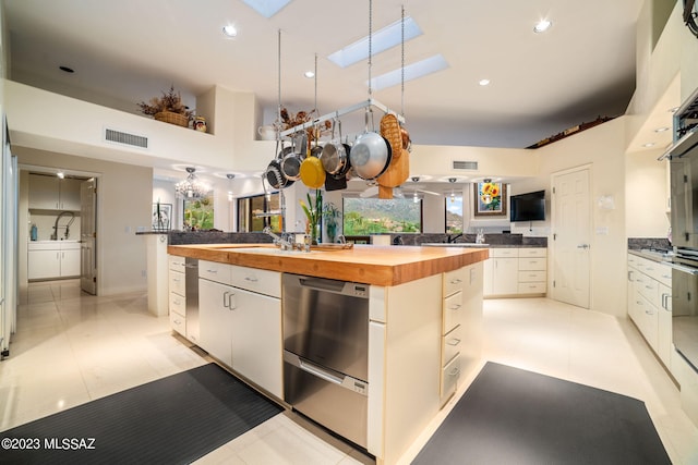 kitchen featuring a skylight, a kitchen island with sink, white cabinets, a high ceiling, and butcher block countertops