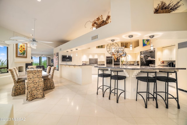 kitchen with pendant lighting, white cabinets, a kitchen breakfast bar, ceiling fan, and light tile patterned floors