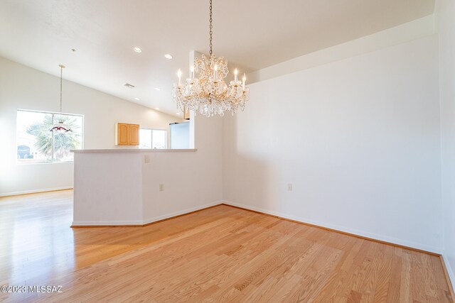 spare room with an inviting chandelier, light hardwood / wood-style floors, and vaulted ceiling