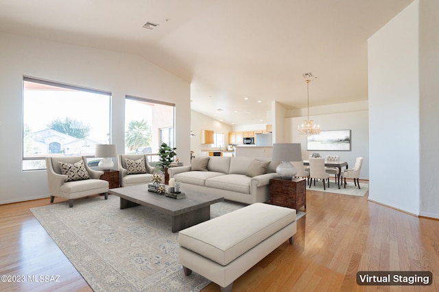 living room with light hardwood / wood-style flooring, a chandelier, and vaulted ceiling