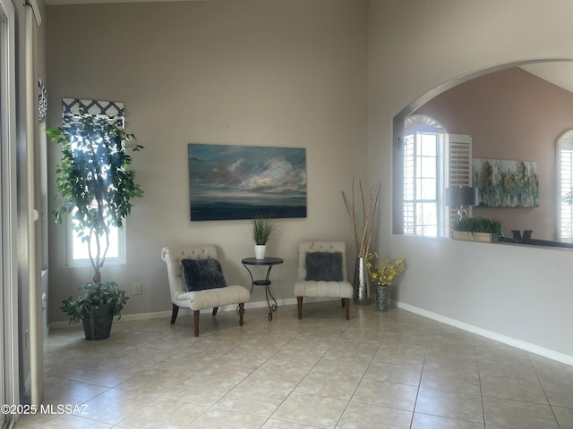 sitting room featuring tile patterned flooring, arched walkways, baseboards, and a towering ceiling