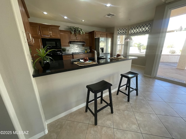 kitchen featuring kitchen peninsula, a breakfast bar area, tasteful backsplash, decorative light fixtures, and black appliances