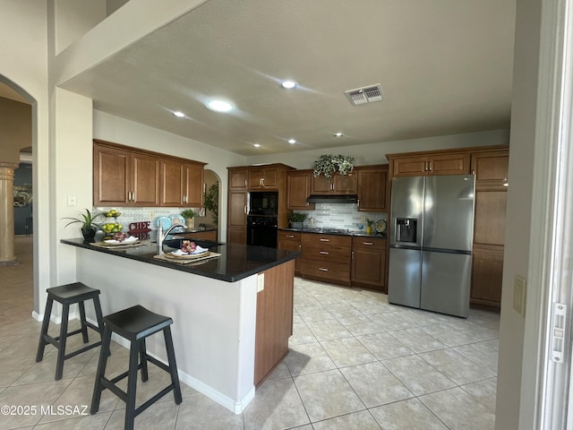 kitchen featuring light tile patterned floors, kitchen peninsula, decorative backsplash, a breakfast bar, and black appliances