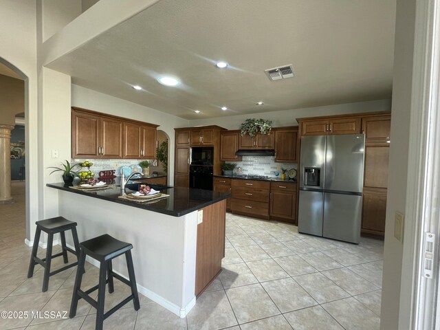 kitchen featuring backsplash, light tile patterned floors, black appliances, and dark stone counters