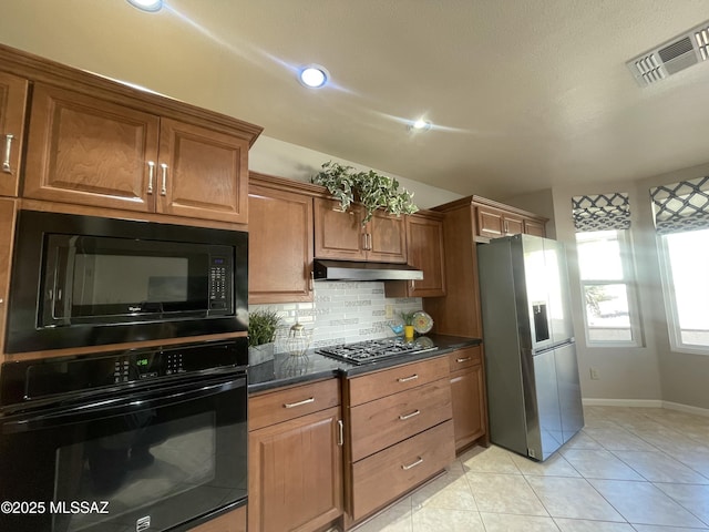 kitchen featuring tasteful backsplash, visible vents, under cabinet range hood, brown cabinets, and black appliances