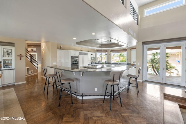 kitchen featuring a tray ceiling, parquet flooring, white cabinets, and a kitchen bar