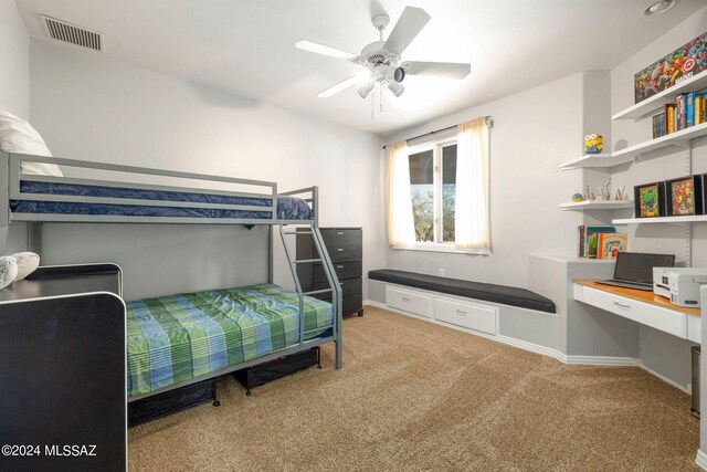 bedroom featuring light colored carpet, built in desk, and ceiling fan