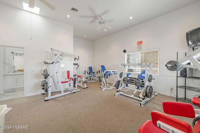 exercise room featuring light colored carpet, sink, a towering ceiling, and ceiling fan