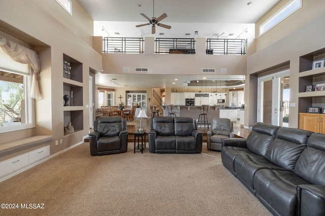 living room featuring built in features, a towering ceiling, carpet flooring, and ceiling fan