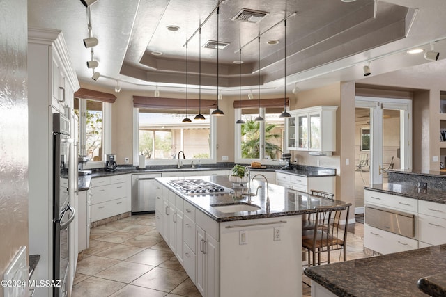 kitchen with pendant lighting, a raised ceiling, sink, a kitchen island with sink, and white cabinetry