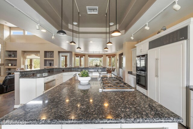 kitchen featuring white cabinetry, hanging light fixtures, dark stone countertops, appliances with stainless steel finishes, and a large island with sink