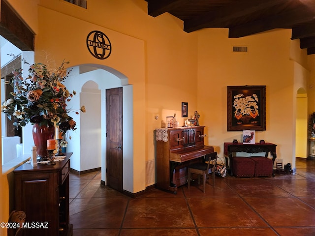 interior space with a high ceiling, beam ceiling, and dark tile flooring