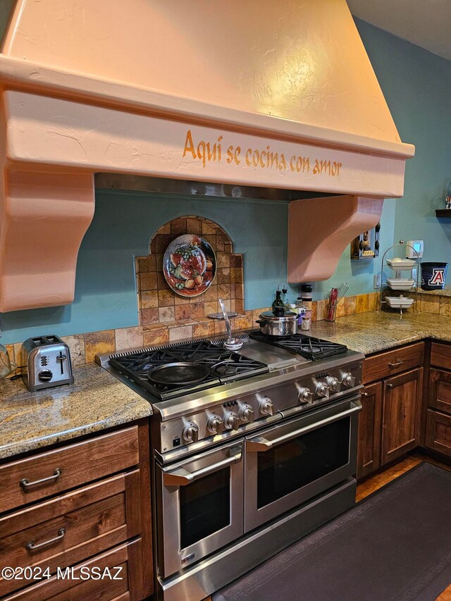 kitchen with light stone counters, premium range hood, and range with two ovens