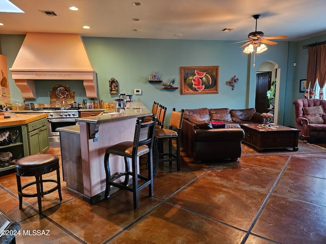 kitchen featuring ceiling fan, a kitchen bar, custom exhaust hood, green cabinets, and range with two ovens