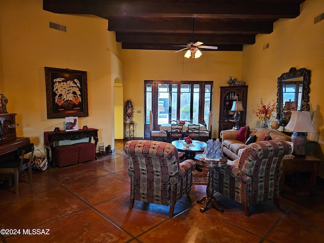 living room featuring dark tile flooring, ceiling fan, a towering ceiling, and beamed ceiling