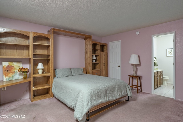 bedroom featuring ensuite bathroom, a textured ceiling, and light colored carpet