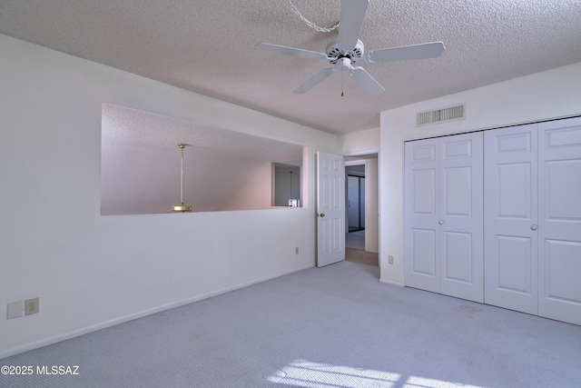 unfurnished bedroom featuring ceiling fan, light colored carpet, a closet, and a textured ceiling