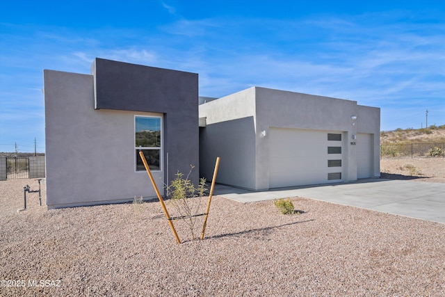 contemporary home with driveway, fence, an attached garage, and stucco siding