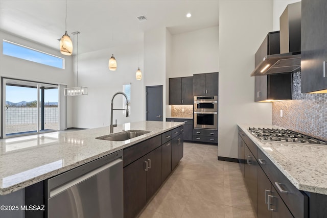 kitchen with visible vents, a towering ceiling, wall chimney exhaust hood, stainless steel appliances, and a sink