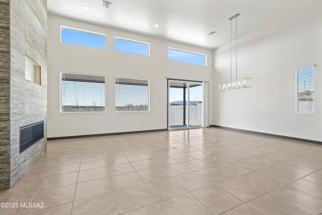 unfurnished living room featuring light tile patterned floors, visible vents, a towering ceiling, a tile fireplace, and baseboards