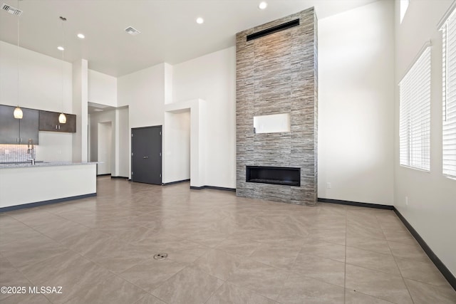 unfurnished living room featuring a fireplace, visible vents, a high ceiling, a sink, and baseboards