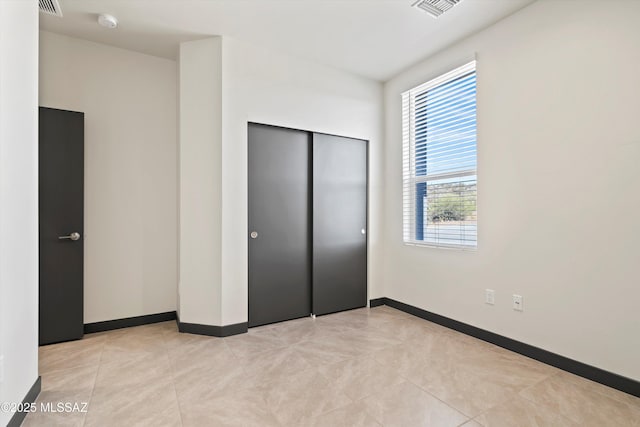 unfurnished bedroom featuring light tile patterned floors, visible vents, baseboards, and a closet