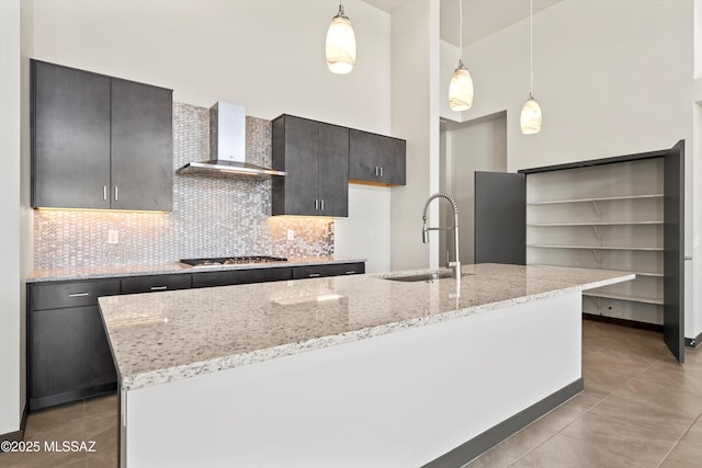 kitchen with stainless steel gas cooktop, a sink, wall chimney range hood, backsplash, and a center island with sink