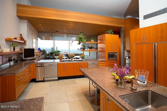 kitchen with light tile flooring, dark stone countertops, decorative light fixtures, sink, and built in appliances