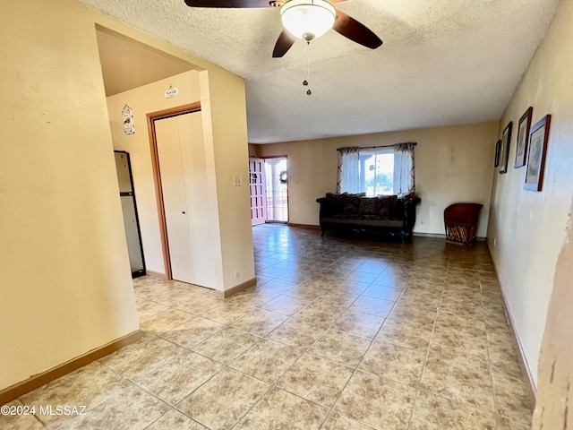 unfurnished living room featuring ceiling fan, light tile patterned floors, and a textured ceiling