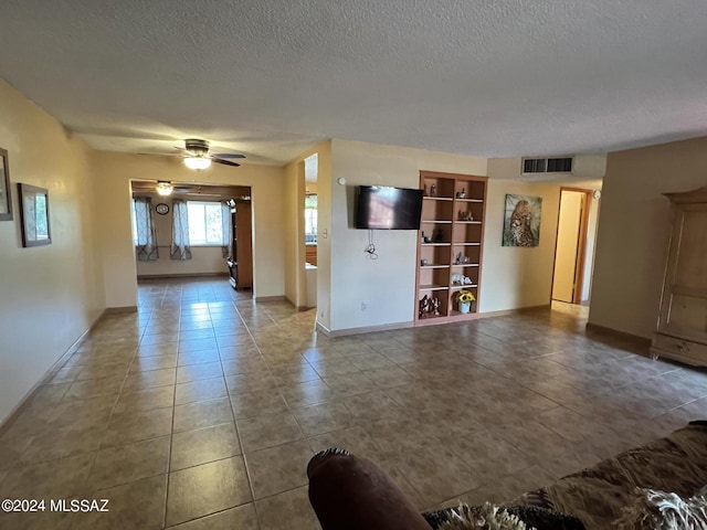 unfurnished living room featuring ceiling fan, built in shelves, tile patterned floors, and a textured ceiling