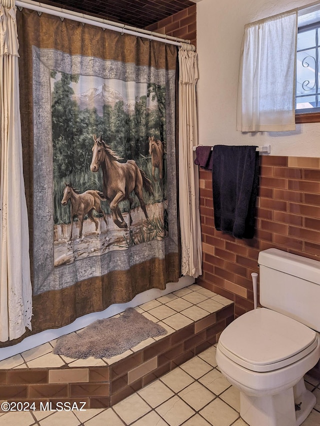 bathroom with tile patterned flooring, brick wall, a shower with shower curtain, and toilet