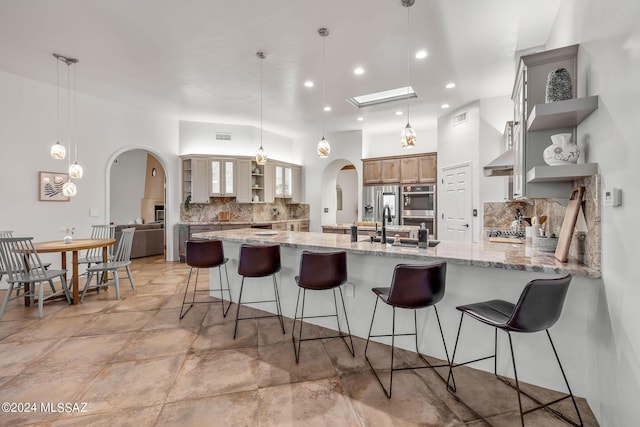 kitchen featuring a breakfast bar area, kitchen peninsula, light stone countertops, and pendant lighting