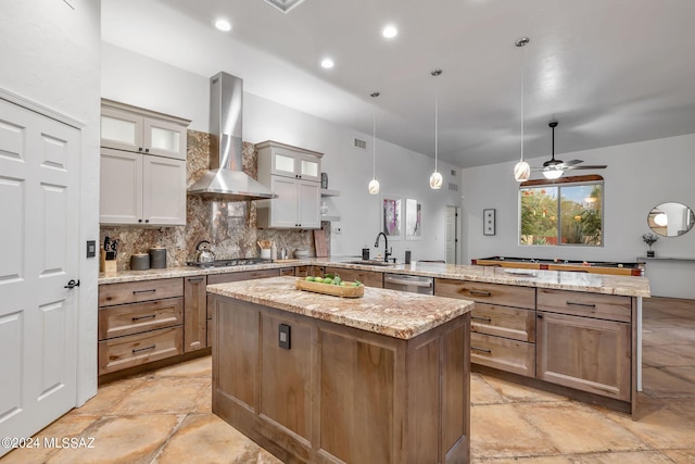 kitchen with kitchen peninsula, sink, wall chimney range hood, pendant lighting, and a kitchen island