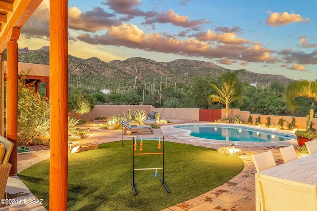 pool at dusk with a lawn, a patio area, and a mountain view