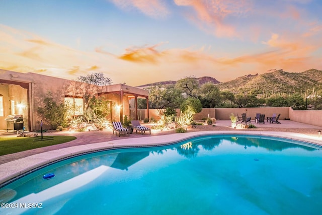 pool at dusk with a mountain view, a patio area, and grilling area