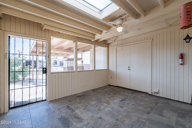 unfurnished sunroom with ceiling fan, beamed ceiling, a skylight, and a healthy amount of sunlight