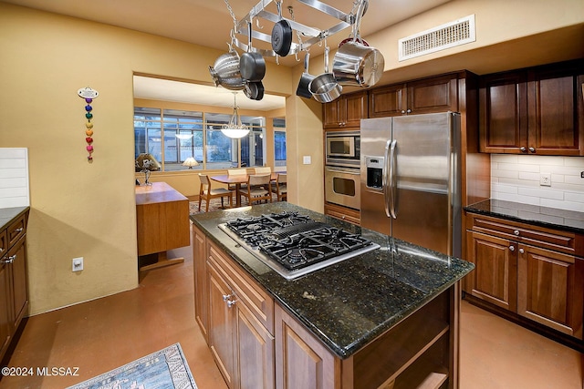 kitchen with appliances with stainless steel finishes, dark stone countertops, backsplash, a kitchen island, and decorative light fixtures