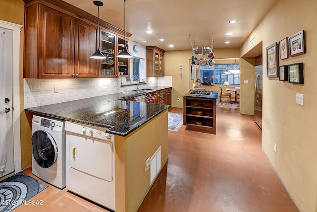 kitchen featuring hanging light fixtures, dark stone countertops, stainless steel refrigerator, kitchen peninsula, and washer / clothes dryer