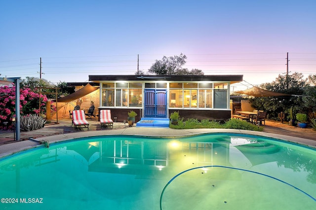 pool at dusk featuring a patio area and a sunroom