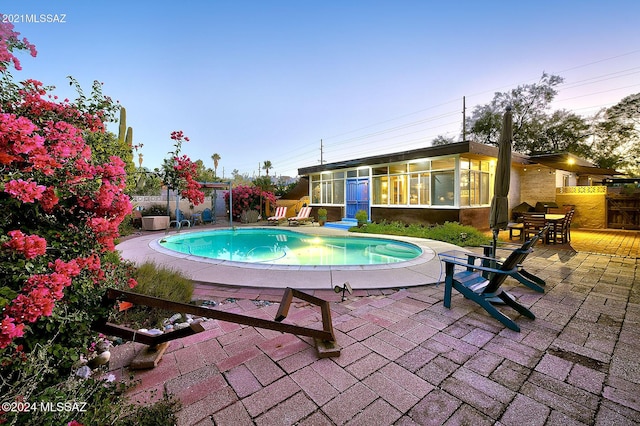 pool at dusk featuring a patio area and a sunroom