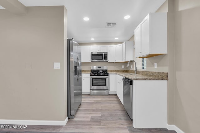 kitchen featuring sink, white cabinetry, light wood-type flooring, appliances with stainless steel finishes, and light stone countertops