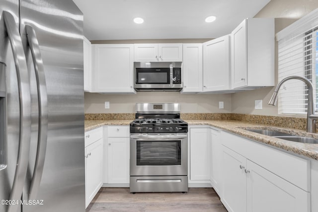 kitchen with light stone counters, sink, stainless steel appliances, and white cabinets