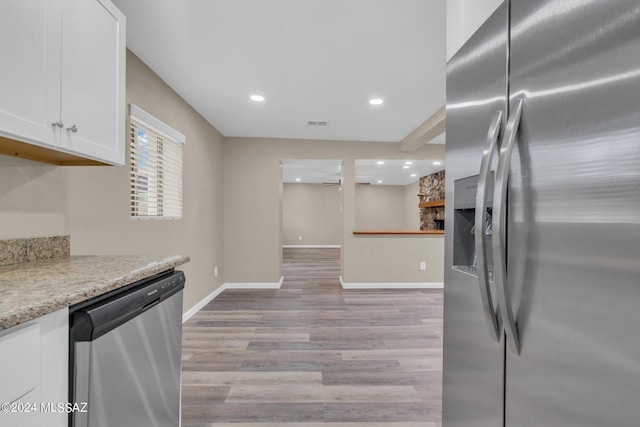 kitchen featuring ceiling fan, appliances with stainless steel finishes, light stone countertops, light hardwood / wood-style floors, and white cabinets