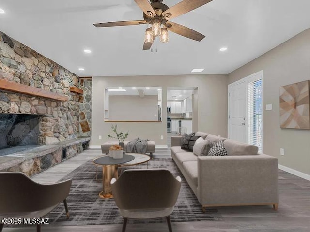 living room with a stone fireplace, dark wood-type flooring, and ceiling fan