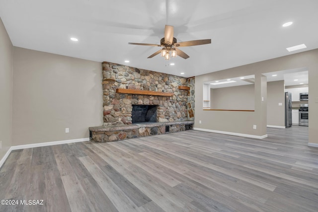 unfurnished living room featuring a stone fireplace, light hardwood / wood-style flooring, and ceiling fan