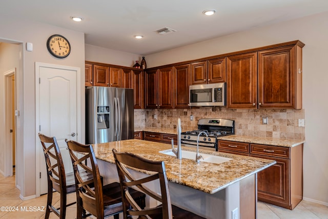 kitchen with light stone countertops, decorative backsplash, stainless steel appliances, a kitchen island with sink, and sink