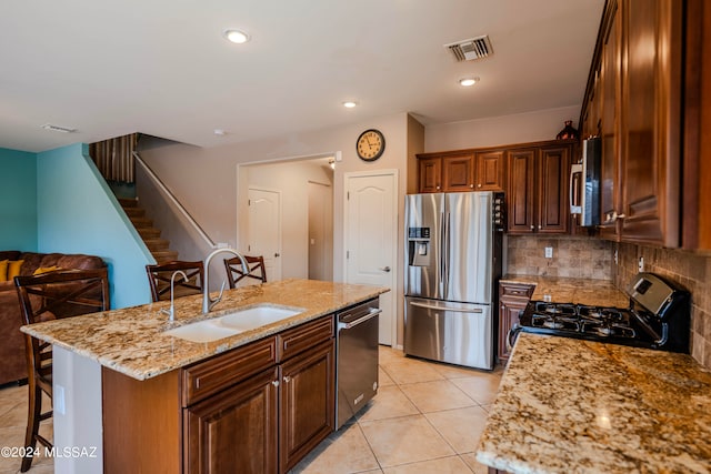 kitchen with light stone countertops, sink, stainless steel appliances, a kitchen bar, and a kitchen island with sink